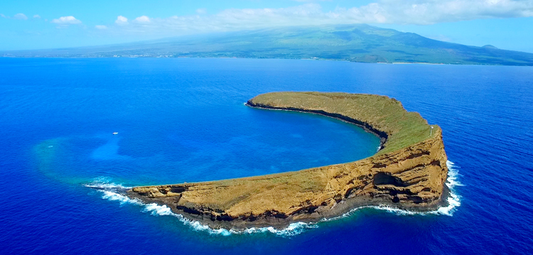 molokini island on a blue sky and ocean day with maui in the background